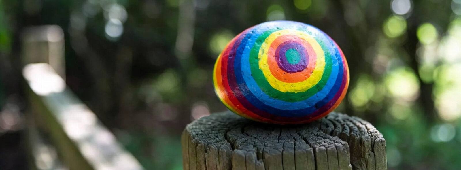 Bunt bemalter Stein auf einem Holzpfeiler im Wald